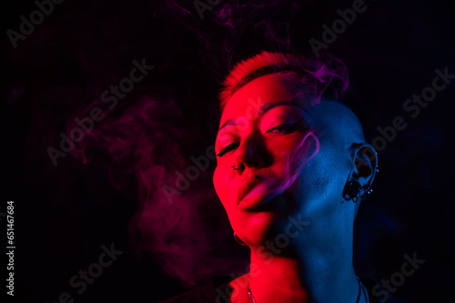 Close up portrait of asian woman with short hair smoking in neon light. 