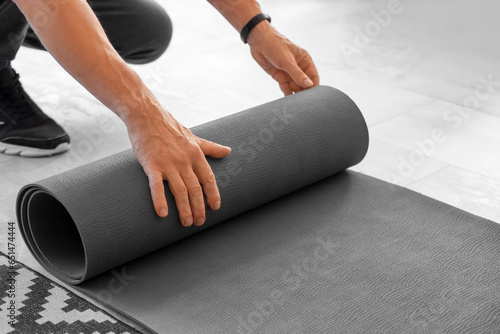 Sporty mature man rolling out fitness mat at home, closeup