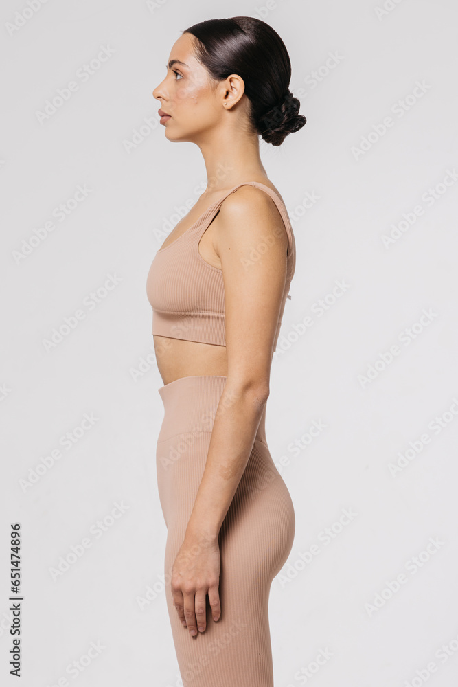 Fototapeta premium A beautiful young woman with a slim figure does sports exercises isolated on a light background. Self-love. The concept of beauty, style, fashion, cosmetology, body and skin care, sports, advertising.