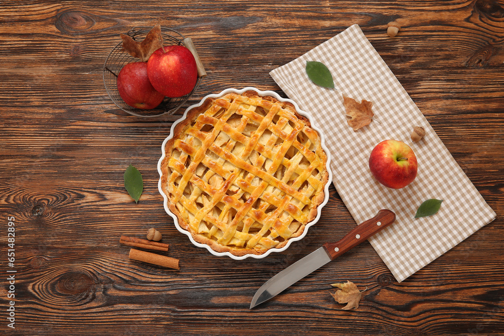 Baking dish with delicious apple pie and cinnamon on wooden background Baking dish with delicious apple pie and cinnamon on wooden background