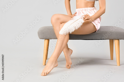 Beautiful woman with shaved legs and feather sitting on light background