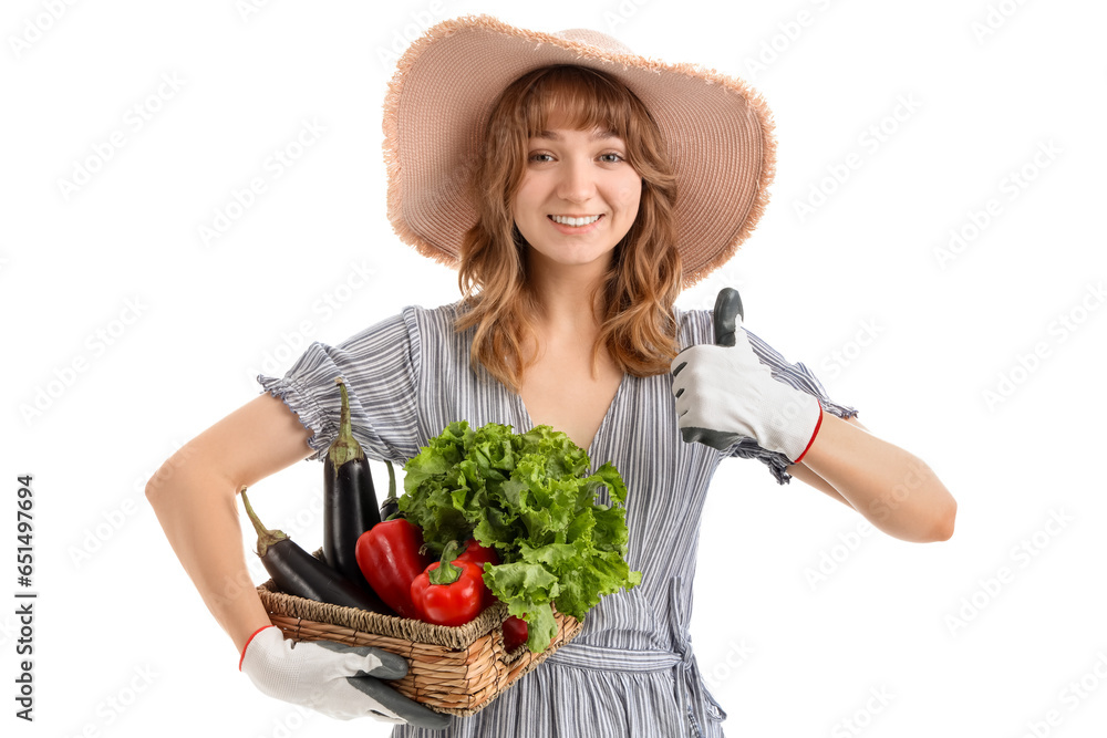 Happy young female farmer with wicker basket full of different ripe vegetables showing thumb-up gesture on white background