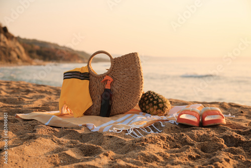 Stylish beach bag, flip-flops, pineapple, sunscreen spray, swimsuit and towel on sand near sea