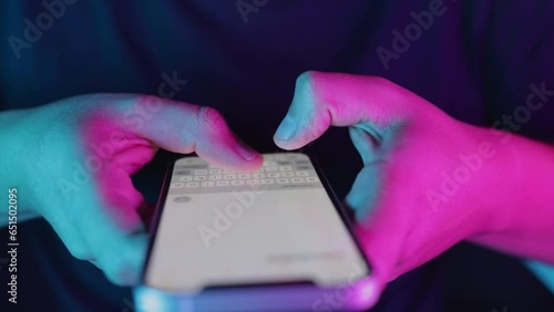 Video of young man's hands writing text on a smartphone neon lights close-up, sending message, current technology