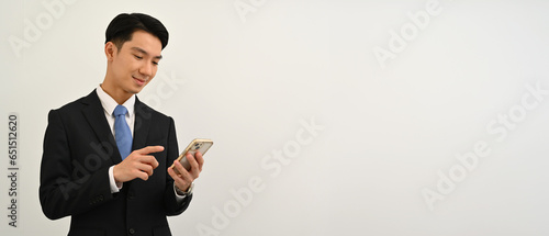 Waist up portrait of Young Asian man in formal suit using mobile phone on white isolated studio background
