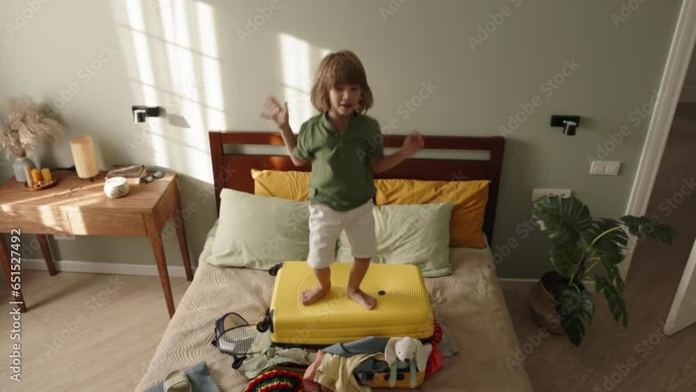 Active child boy jumping on suitcase. Bag luggage with poorly packed