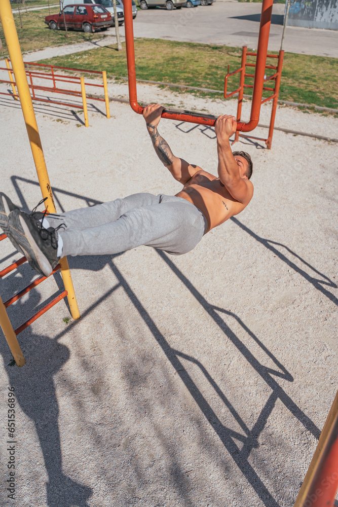 Man working out in the park while hanging on a bar. Hanging leg raises