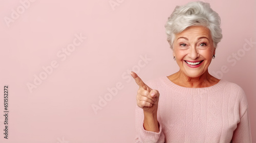 Senior beautiful woman pointing aside and smiling with pink background and copy space photo