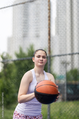 Girl playing basketball. Player throwing ball. Outdoor sports field in urban surroundings.