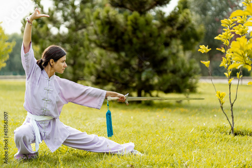 Martial arts woman practicing wushu kung-fu with sword at green park