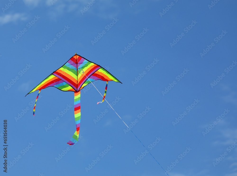 colorful kite of many colors of the rainbow flies tied to a thread in the blue sky symbol of childhood and carefreeness