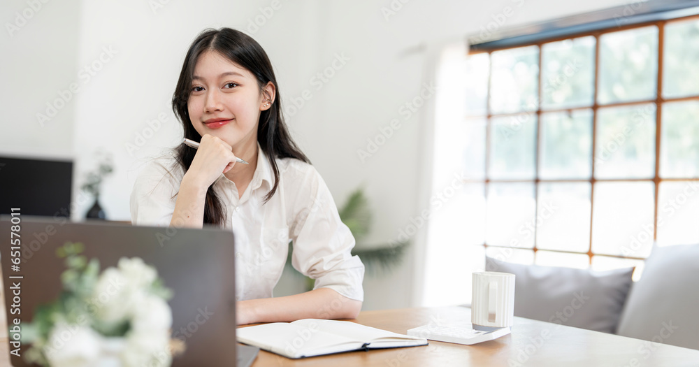 Smiling woman sitting at her desk in office. Happy business woman sitting in office with fingers touching her chin.