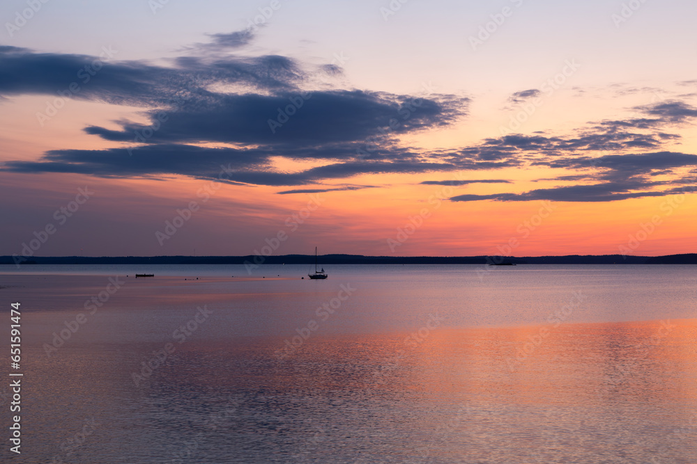 Tiny sailboat anchored in Frenchman Bay during a pink and orange sunrise, Bar Harbor, Maine, USA
