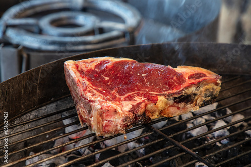 T-Bone steak on the grill raw. The smoke can be seen in the picture. Picture taken outdoors.