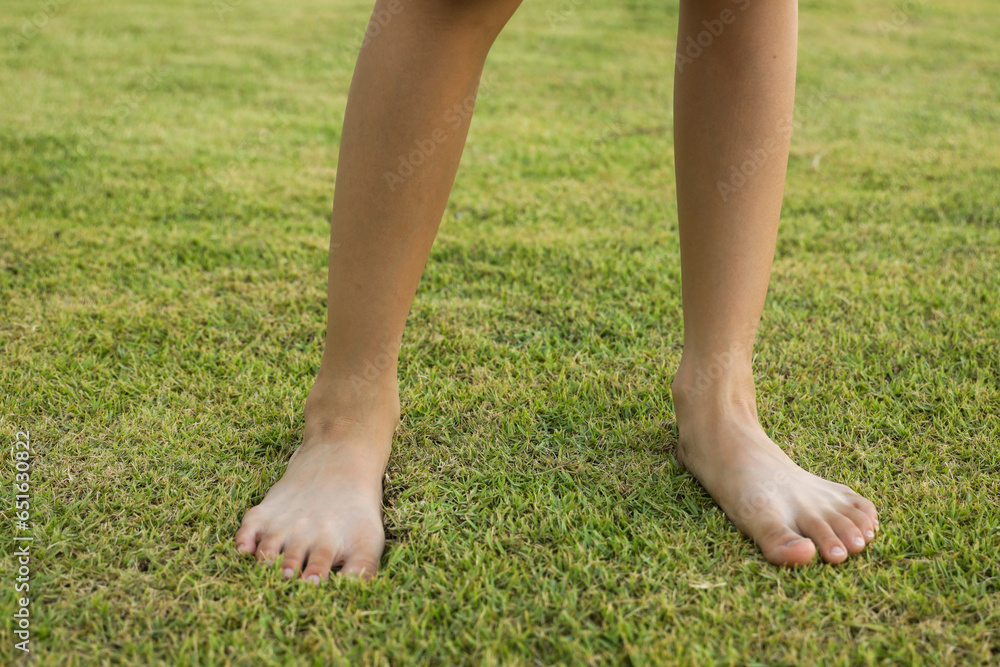 Children's feet are walking barefoot on the green grass. Self-massage on natural surfaces to correct curvature.