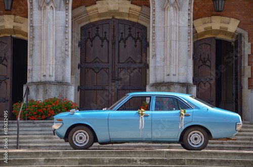 An antique blue car standing in front of the church, decorated with flowers - a wedding car © Pawel Filusz
