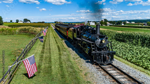 An Aerial View of a Steam Passenger Train Approaching, on a single Track With a Fence and America Flags Blowing in the Wind, on a Summer Day photo