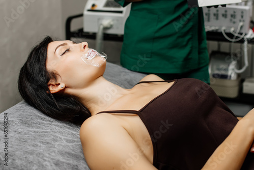 Cosmetology clinic, the doctor applies anesthesia to the patient's lips, anesthetic before injecting hyaluronic acid. Anesthetic ointment is applied before the injection procedure.