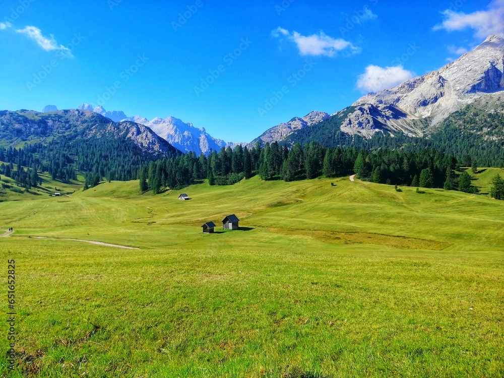 A landscape of green meadows on a sunny summer day in the Dolomites, Italy. Green pasture and small farm huts in a valley in South Tyrol.
