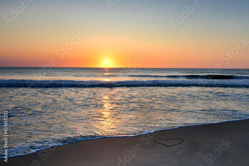 Heart drawn in the sand on the beach at sunrise over the ocean