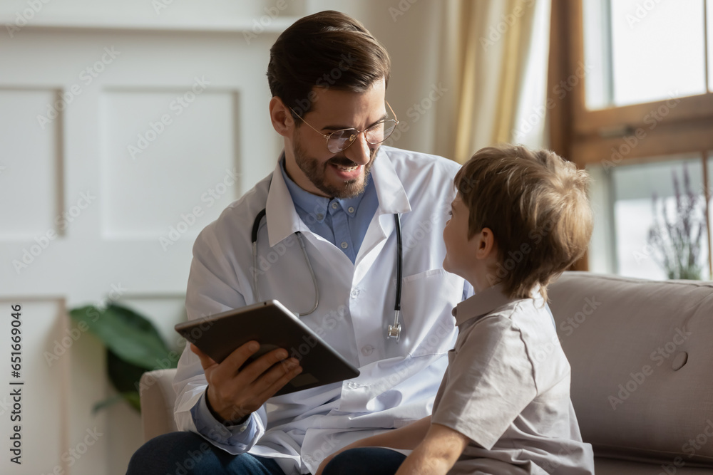 Smiling pediatrician using tablet at medical appointment with little boy, positive doctor wearing glasses filling patient card, anamnesis, showing good medical checkup results, children healthcare - obrazy, fototapety, plakaty 