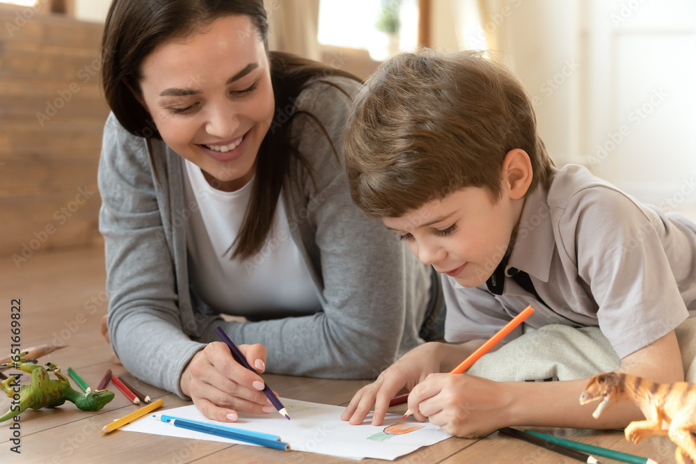 Close up happy mother and little son drawing colorful pencils on paper sheet together, having fun, lying on warm wooden floor with underfloor heating, family enjoying creative activity at home Close up happy mother and little son drawing colorful pencils on paper sheet together, having fun, lying on warm wooden floor with underfloor heating, family enjoying creative activity at home