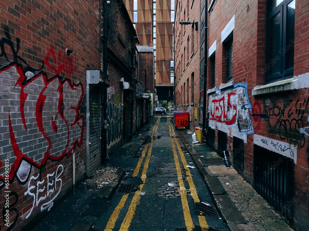 Naklejka premium Alley way in Manchester England with bins rubbish / trash and random graffiti on the wall.