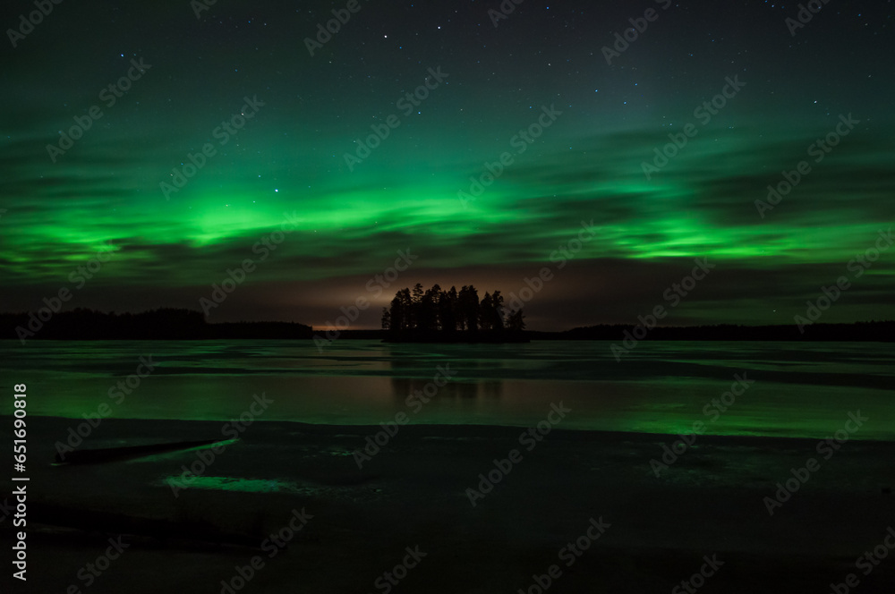 Naklejka premium Island in the middle of a frozen lake with the sky colored green by aurora boralis light in winter in Pirkanmaa, Finland