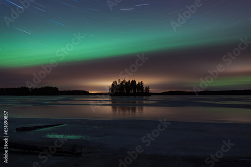 Island in the middle of a frozen lake with the sky colored green by aurora boralis light in winter in Pirkanmaa, Finland