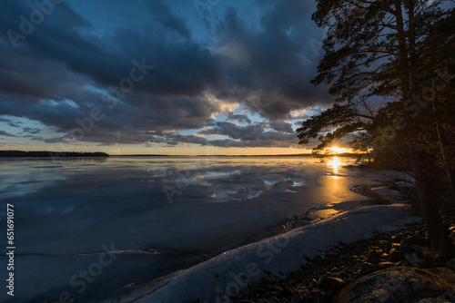 View of a frozen lake with clouds in the sky around sunset time in late winter in Finland
