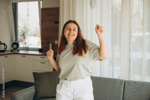 Portrait of happy woman dancing, rejoicing and triumphing, feeling upbeat at home. Copy space. Young female enjoying carefree and leisure weekend