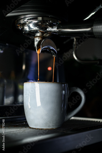 Close up view on process of pouring strong hot espresso to small white cup from professional coffee machine
