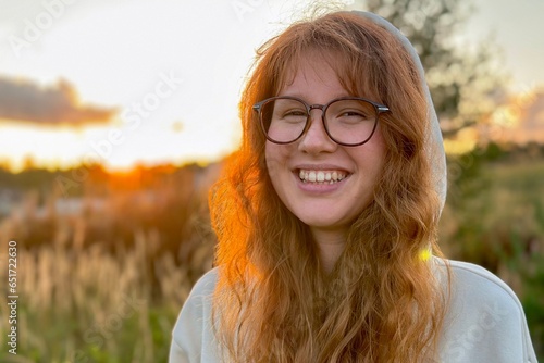 Portrait of happy young woman in glasses at sunset on natural background smile and looking at camera. 