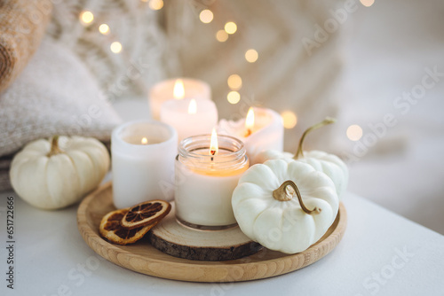 Autumn home decor with white pumpkins and burning aroma candles with sweet spicy pumpkin pie scent. Cozy fall composition  relaxation  aromatherapy. Apartment design  living room or bedroom