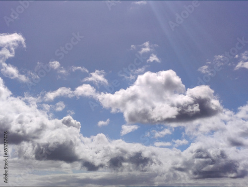 White clouds in the summer sun rays over blue sky background. Fluffy cumulus cloudscape shape