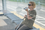 Elderly blind woman sitting at a bus stop and using a smartphone. 