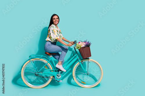 Full length photo of lovely pretty girl wear stylish outfit having fun riding bicycle empty space isolated on bright cyan color background © deagreez