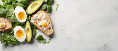 Top down view of bread with fried eggs avocado and greens on a light stone background