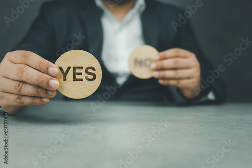 Businessman hand making a choice of Yes from between two cubes with Yes and No. Voting yes or positive decision to accept. The opposite words yes or no on circle block.