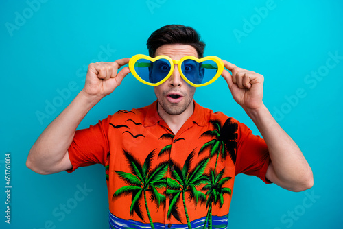 Photo of impressed astonished man with stylish hairdo dressed print shirt hold funny glasses open mouth isolated on blue color background