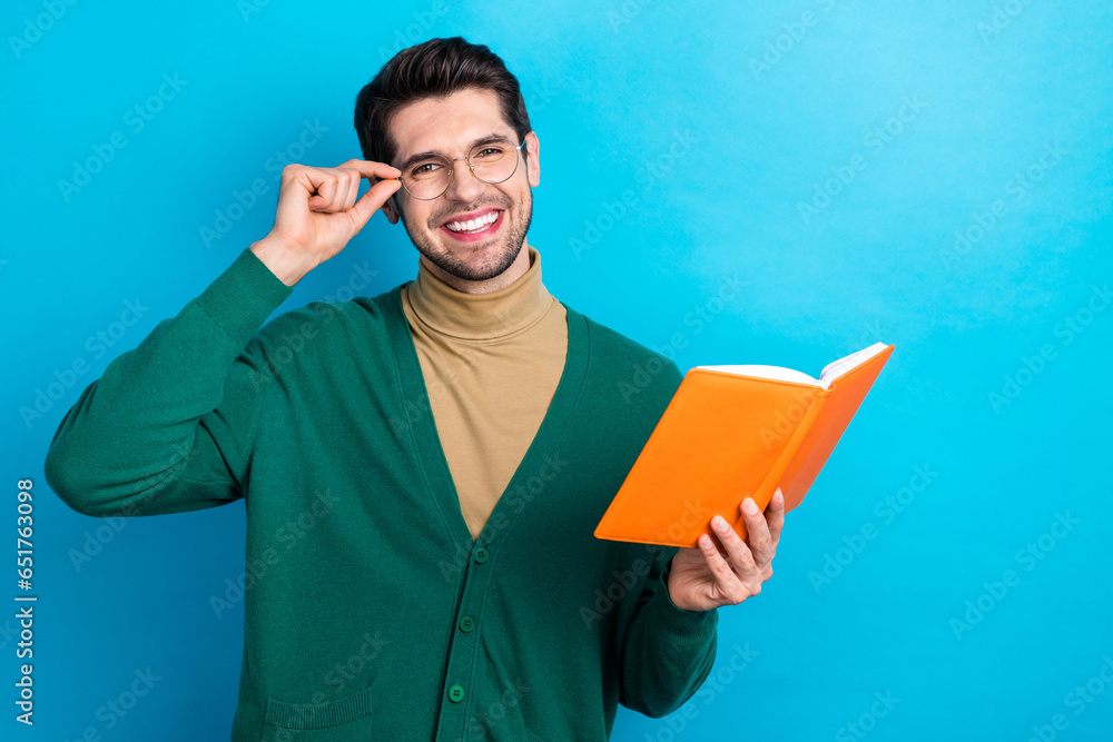 Photo of young man brunet wear green cardigan touch his glasses holding red diary copybook intellectual isolated on blue color background Photo of young man brunet wear green cardigan touch his glasses holding red diary copybook intellectual isolated on blue color background