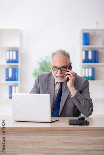 Old male employee talking by phone at workplace