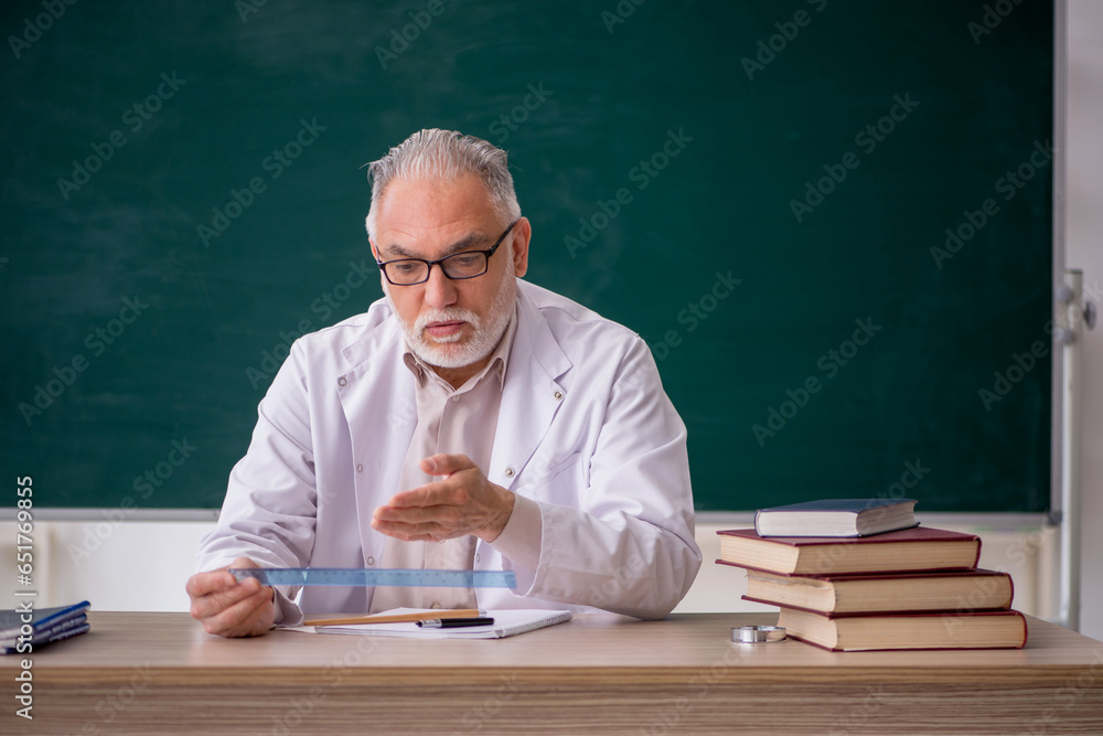 Old male teacher in front of green board Old male teacher in front of green board