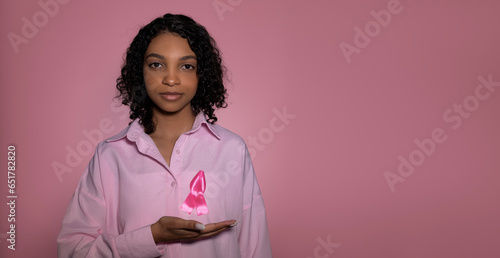 Copy space banner with breast cancer awaraness concept. Young survivor pointing at pink ribbbon. Background with place for text photo