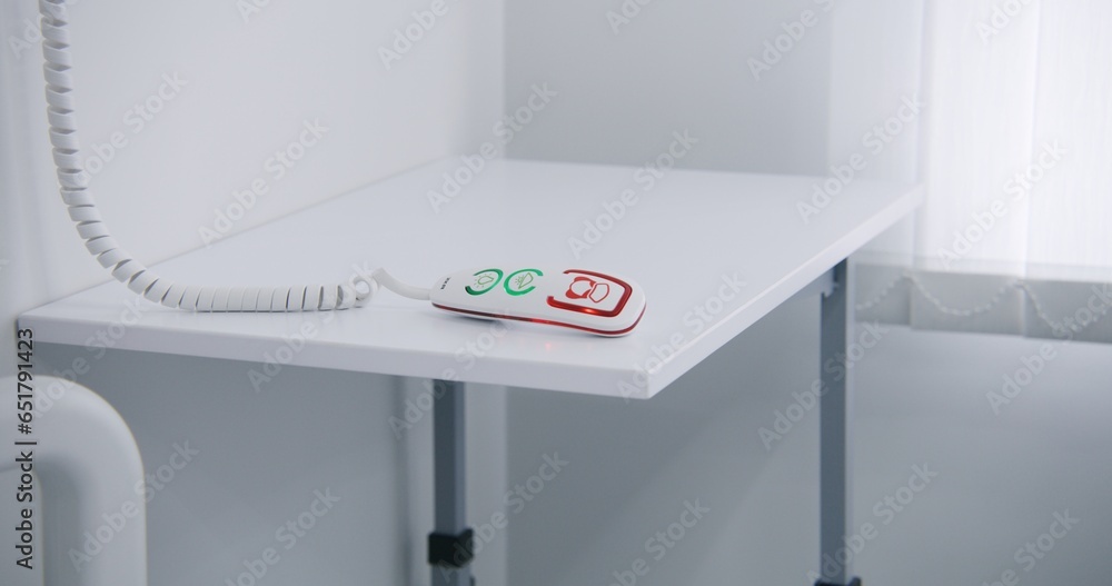 Close up shot of remote control with nurse calling system lying on white bedside table in bright hospital ward near window. Modern equipment in clinic or medical facility for comfort of patient.