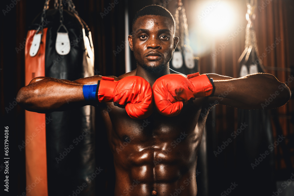 Boxing fighter posing, African American Black boxer put his hand or fist wearing glove together in front in aggressive stance and ready to fight at gym with kicking bag and boxing equipment. Impetus