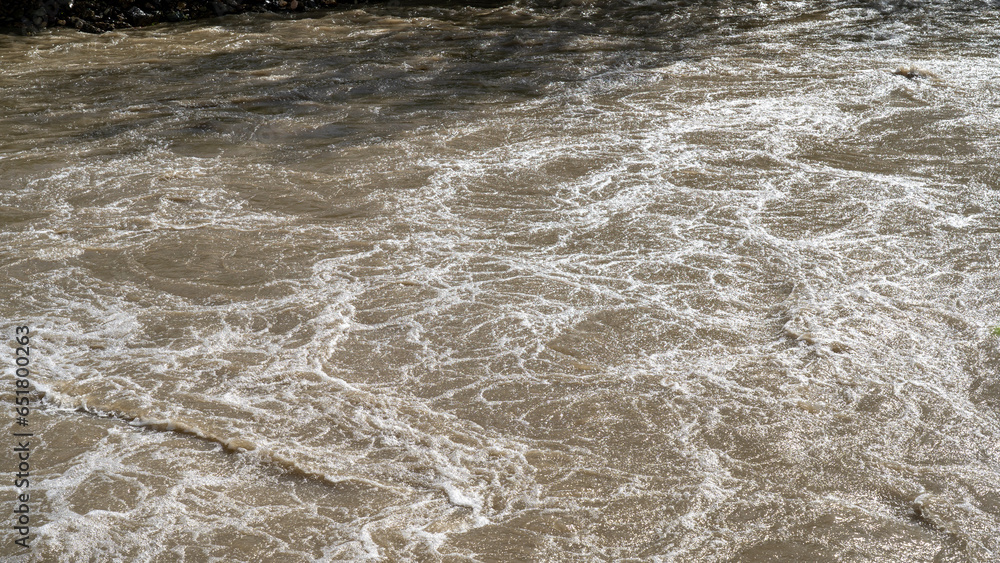 The river swollen after heavy rainfall and flood water crashing through valley. The water flows fast from the high valley to the plain. General contest of a river in flood The river swollen after heavy rainfall and flood water crashing through valley. The water flows fast from the high valley to the plain. General contest of a river in flood