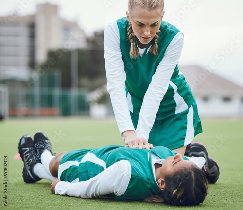 First aid, cpr and emergency with a hockey player on a field to save a player on her team after an accident. Fitness, training and heart attack with a woman helping her friend on a field of grass