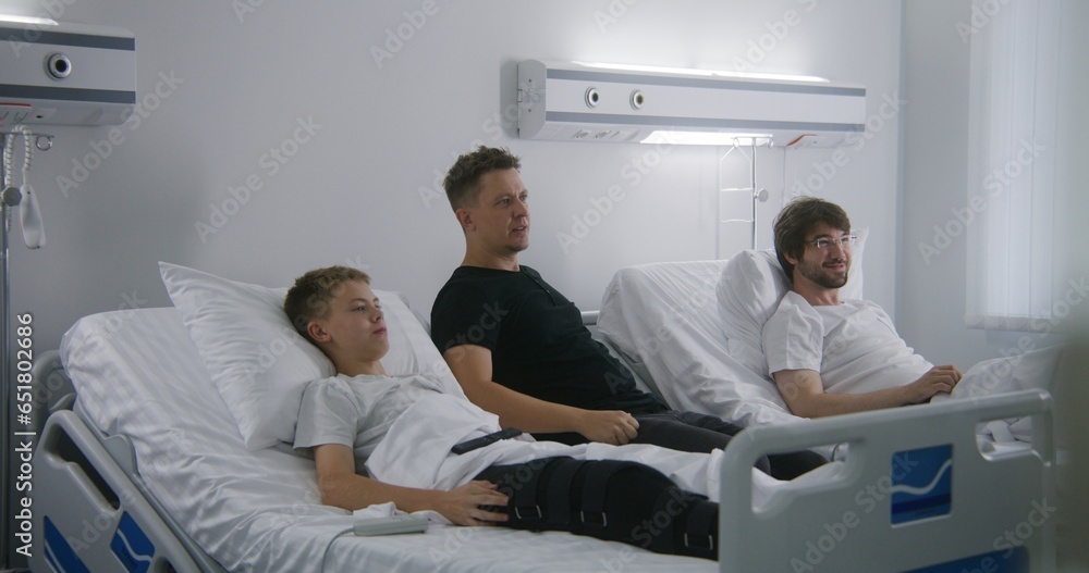 Father, kid and neighbor patient rest in hospital ward and emotionally watching sports championship. Hospital roommates fully recovering after successful surgery. Father, kid and neighbor patient rest in hospital ward and emotionally watching sports championship. Hospital roommates fully recovering after successful surgery.