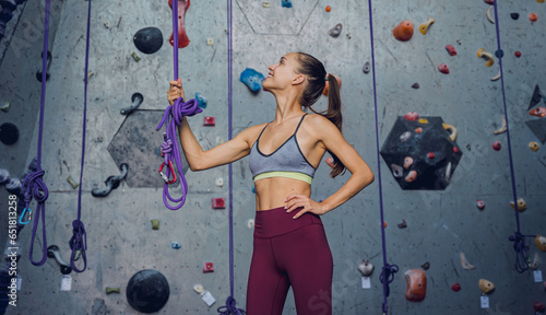 A strong female climber against an artificial wall with colorful grips and ropes.